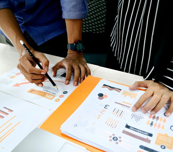 Hands analyzing colorful reports and charts on a table, illustrating website analytics and performance metrics relevant to Mbvelo IT Consulting's services.